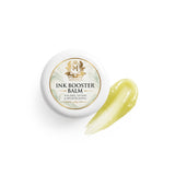 Skin Monarch Ink Booster Balm 30ml, καπάκι δίπλα σε δείγμα γυαλιστερού κίτρινου βάλσαμου